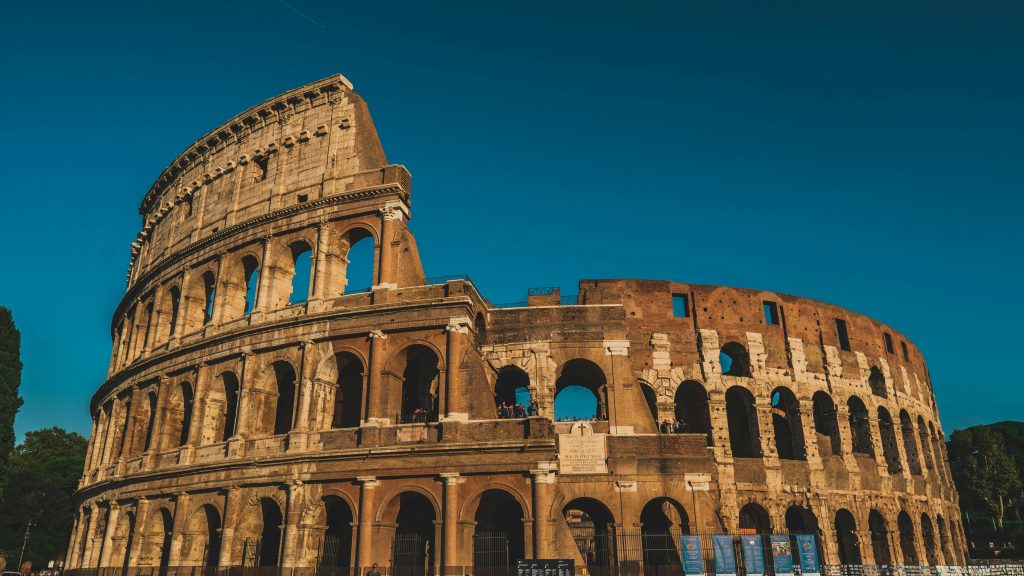 This image beautifully captures the grandeur of the Colosseum in Rome, Italy, bathed in the warm glow of the setting sun. The ancient amphitheater, an iconic symbol of Roman engineering and architecture, stands against a clear blue sky, highlighting its historic arches and weathered stone facade. Ideal for travel enthusiasts and history buffs, this photo showcases one of the world's most renowned landmarks, inviting viewers to explore the rich cultural heritage of Rome.