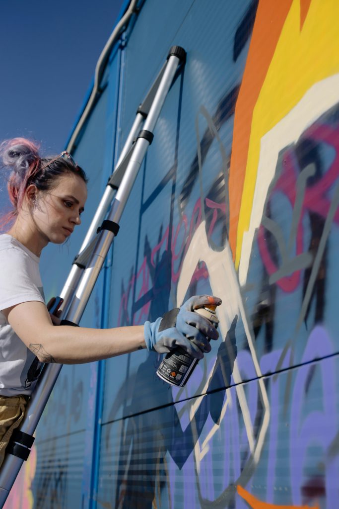 In this photo, an artist demonstrates various **street art techniques and styles** while working on a vibrant mural. The image showcases the creativity and skill involved in street art, highlighting the intricate process of layering colors and shapes to create a striking visual piece.