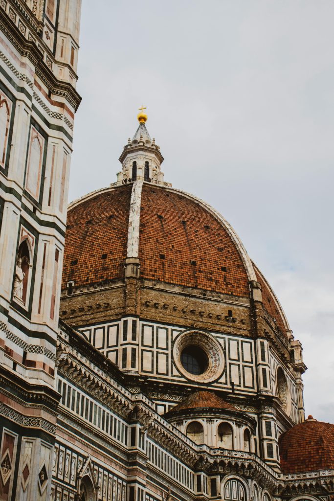 This image captures the stunning architectural beauty of the Florence Cathedral, also known as the Duomo di Firenze, in Italy. The focus is on the cathedral's magnificent red-tiled dome, designed by Filippo Brunelleschi, which is an iconic symbol of Renaissance architecture. The intricate details of the cathedral’s facade, featuring geometric patterns and statues, add to the grandeur of this historical masterpiece. The overcast sky provides a neutral backdrop, emphasizing the structure’s rich textures and colors. Ideal for travel enthusiasts, history buffs, and architecture lovers, this image showcases one of the world's most renowned architectural landmarks.